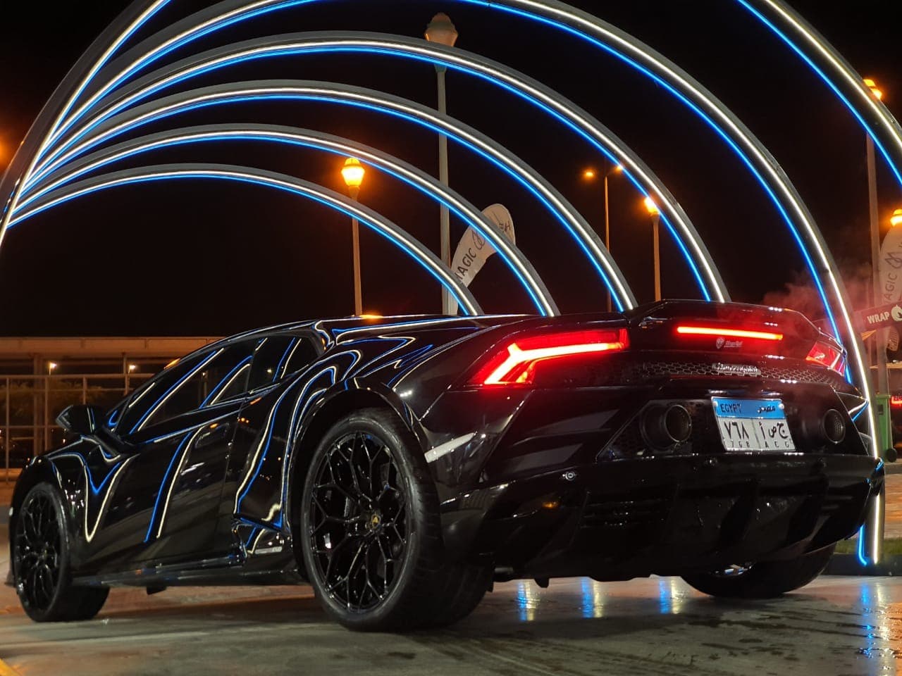 Black Lamborghini Huracán under neon light arches at Magic Wash