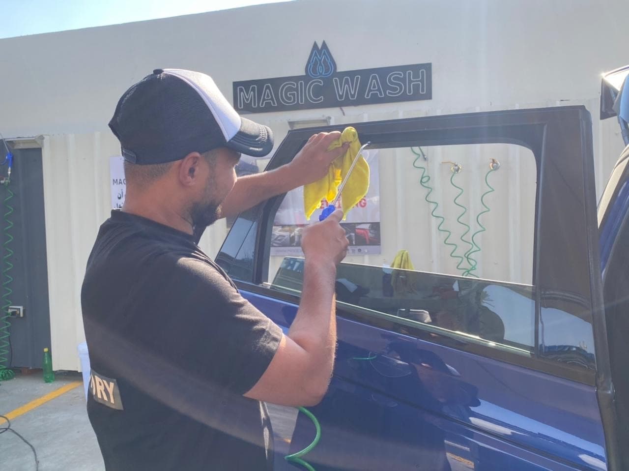 Staff drying a car window beside the neon Magic Wash sign